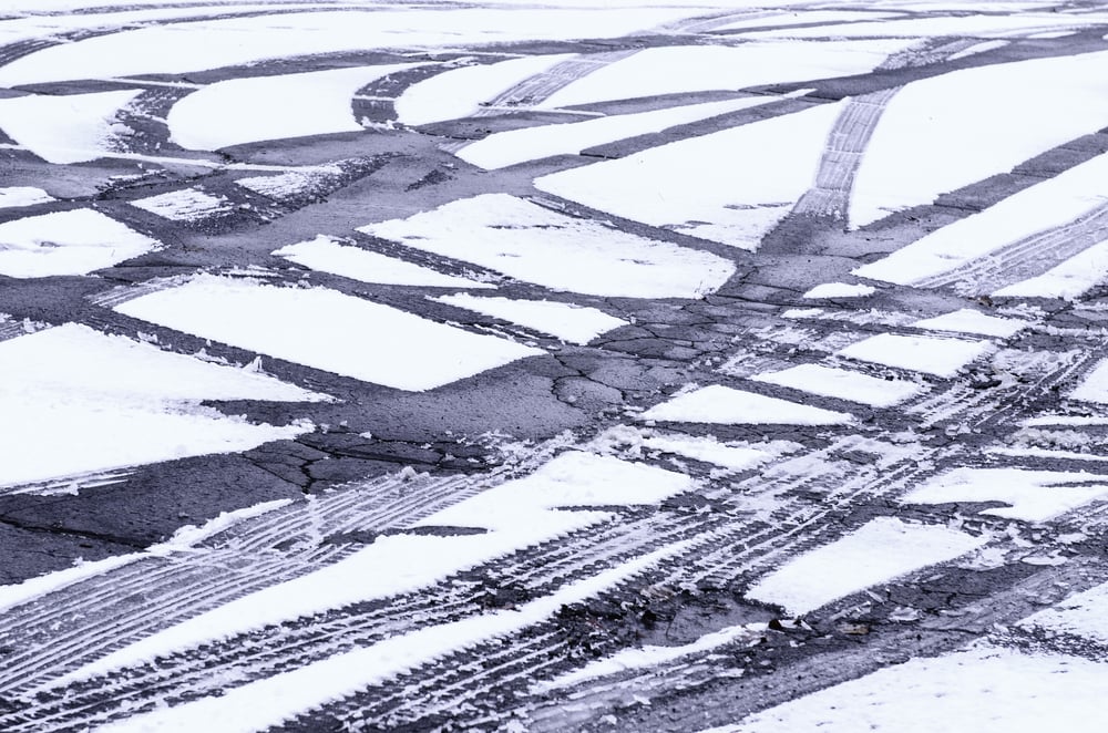 Winter at a glance Fresh tire tracks intersecting in light snow on asphalt pavement of parking lot